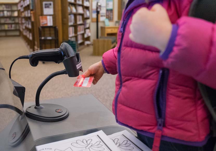 young patron checking out book with library card
